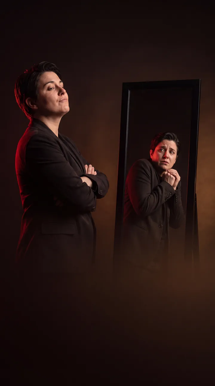 A person stands proudly with arms crossed. Their reflection in the mirror looks small and scared.